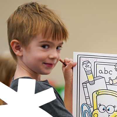 Elementary school student proudly showing a colorful drawing of a school bus and pencils in a Bellingham classroom, supported by the Bellingham Public Schools Foundation.