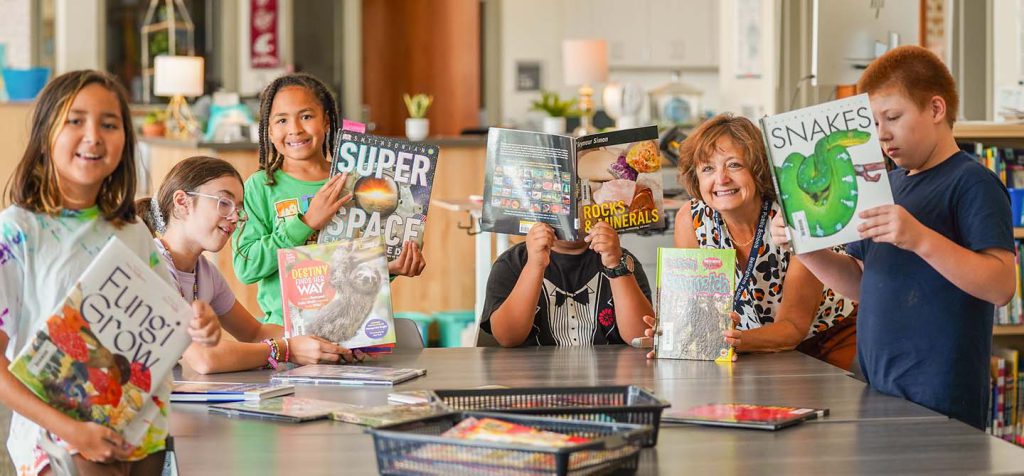 Kids holding library books and smiling at the camera